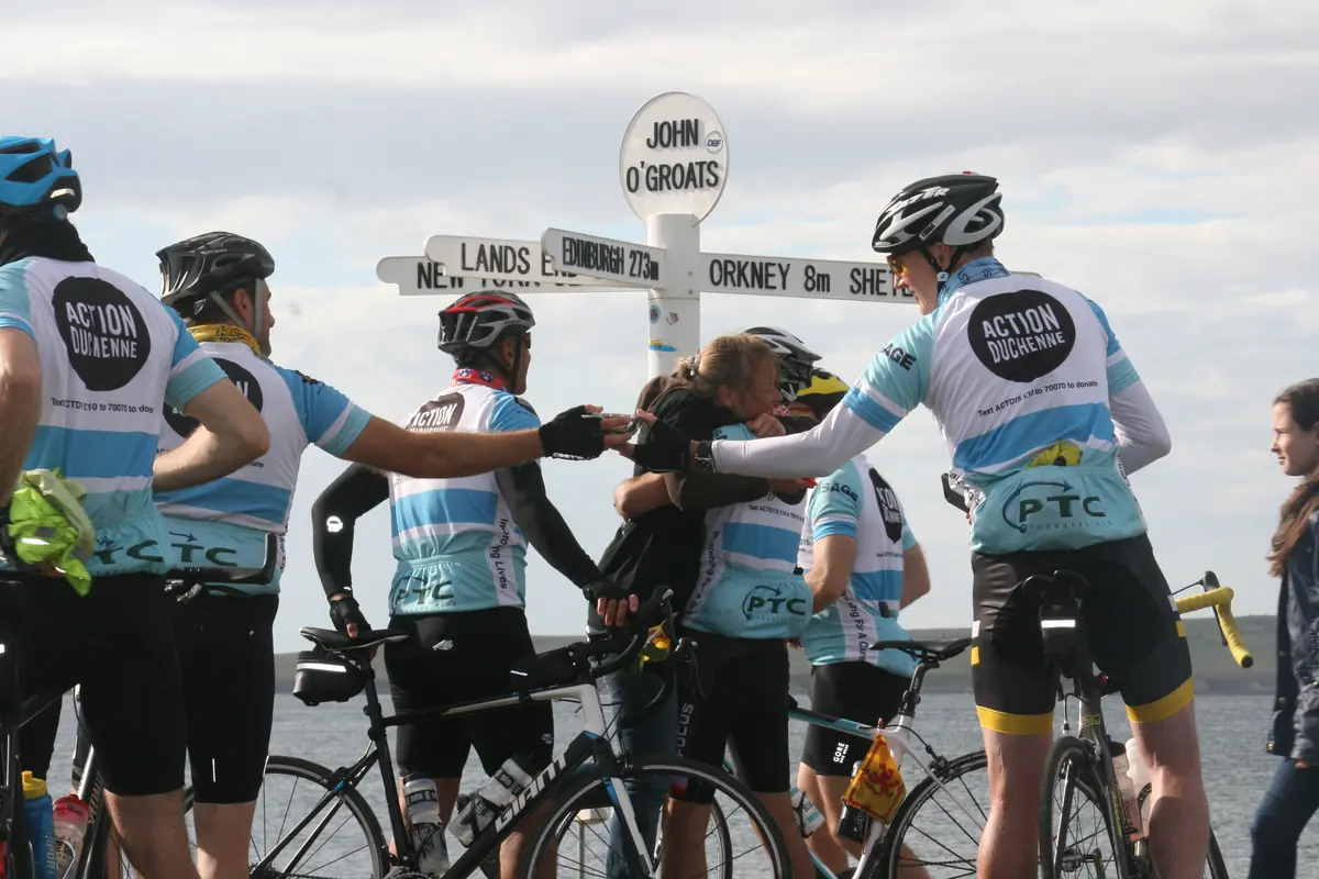 Action Duchenne charity riders celebrating at the John O'Groats signpost after cycling from Land's End