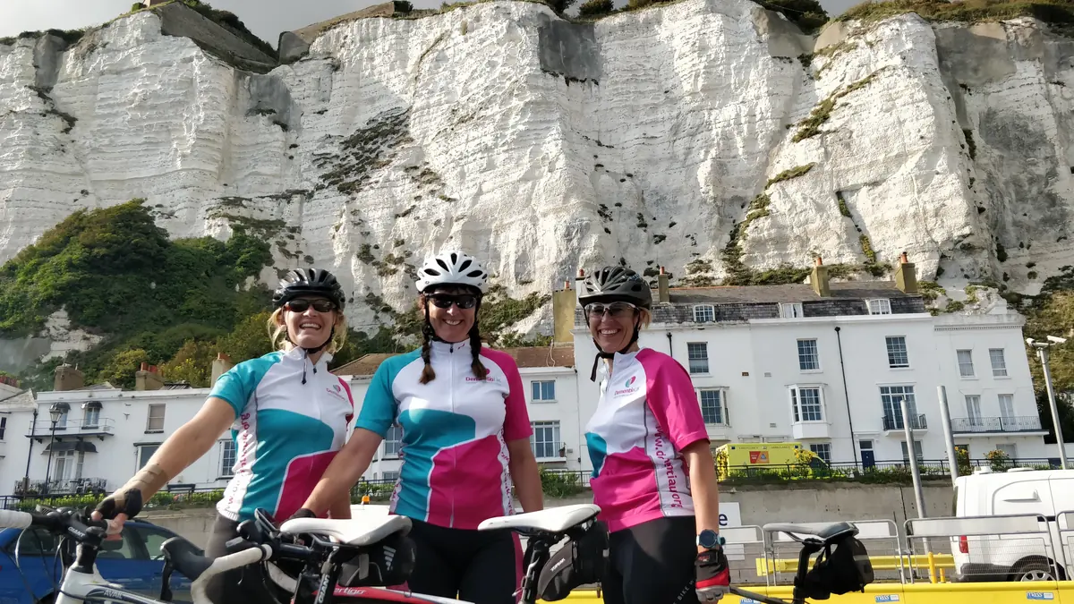 Three Dementia UK charity cyclists in matching jerseys below the white cliffs of Dover