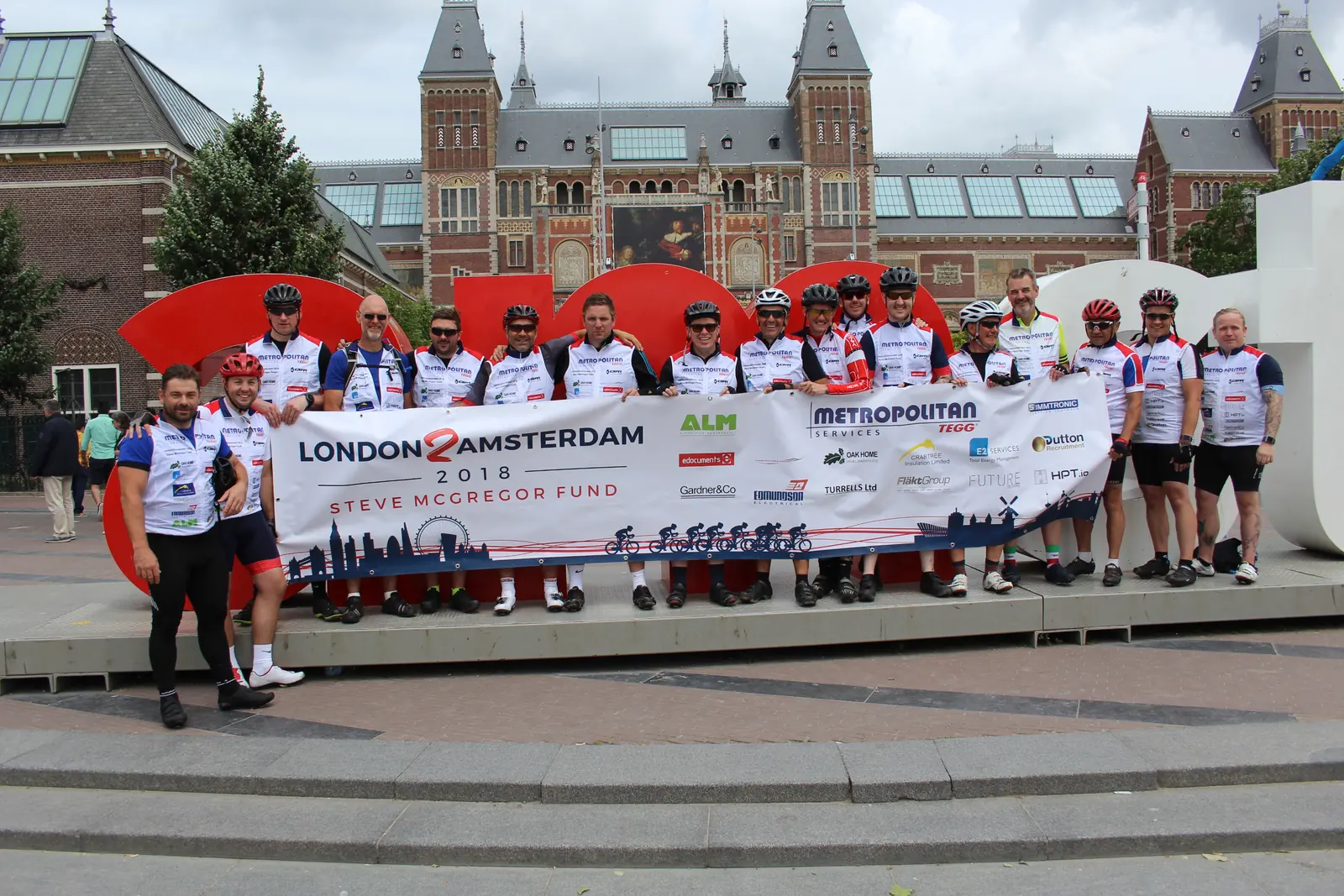 A large charity cycling team with their banner outside the Rijksmuseum at the finish of a London to Amsterdam ride