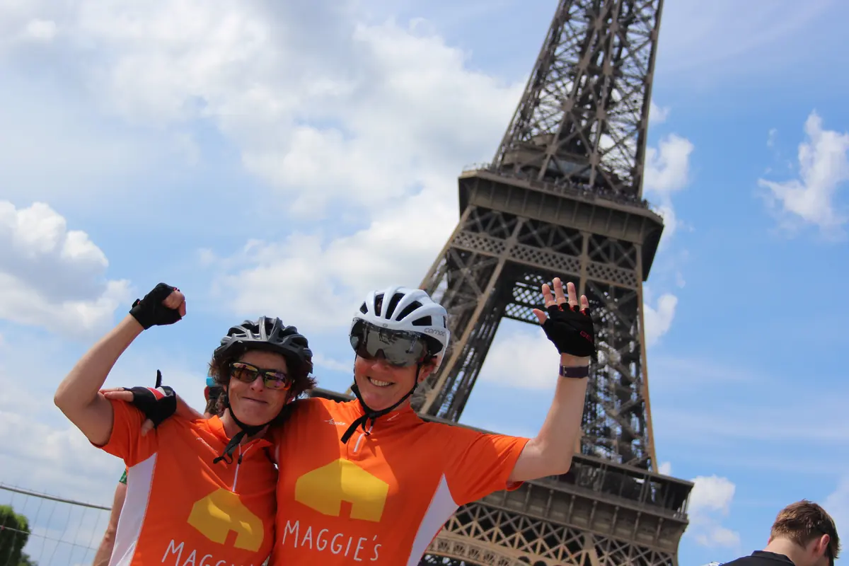 Two Maggie's charity riders in orange jerseys celebrating under the Eiffel Tower