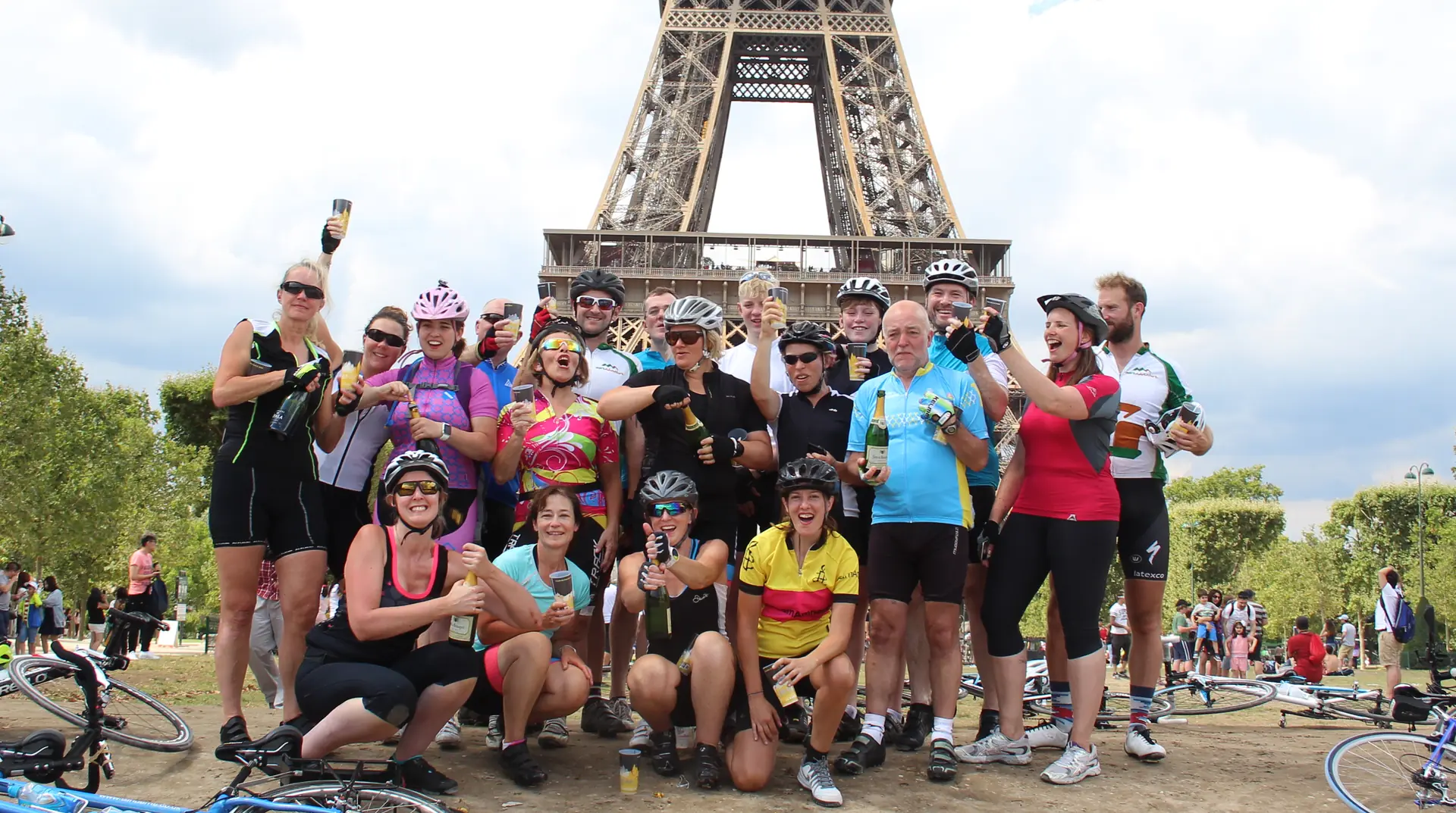 London to Paris cyclists celebrating with champagne under the Eiffel Tower at the end of their More Adventure bike ride