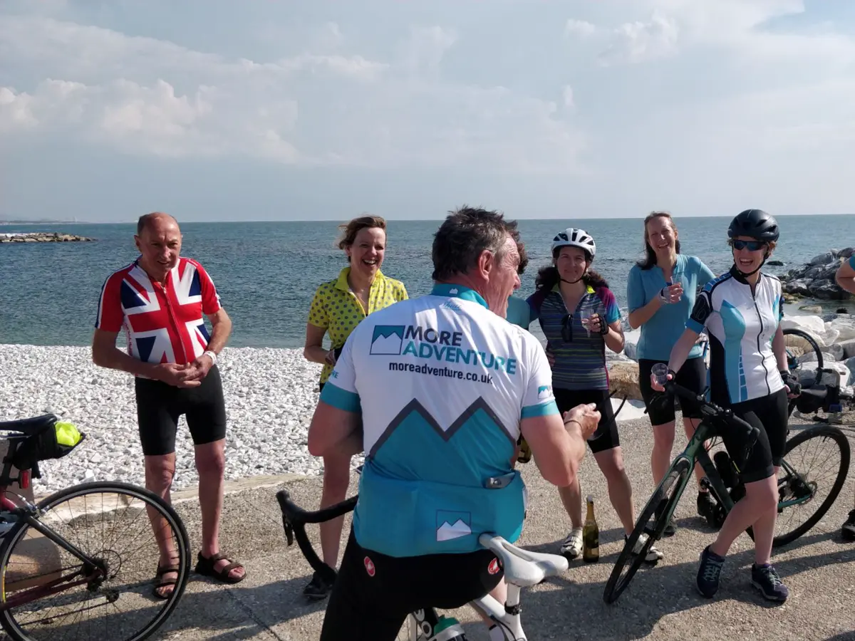 A More Adventure leader toasting a group of smiling cyclists on a Mediterranean seafront