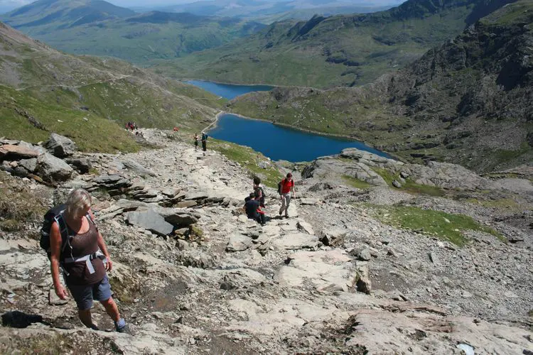 A hiker on a rocky mountain path above a lake in Eryri (Snowdonia)