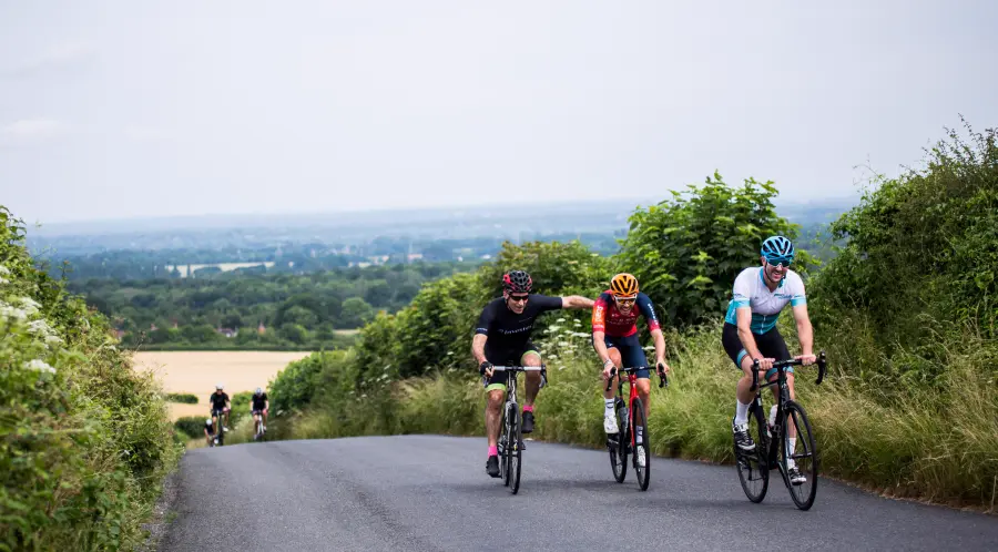Charity cyclists tackling a climb on a country road with sea views behind