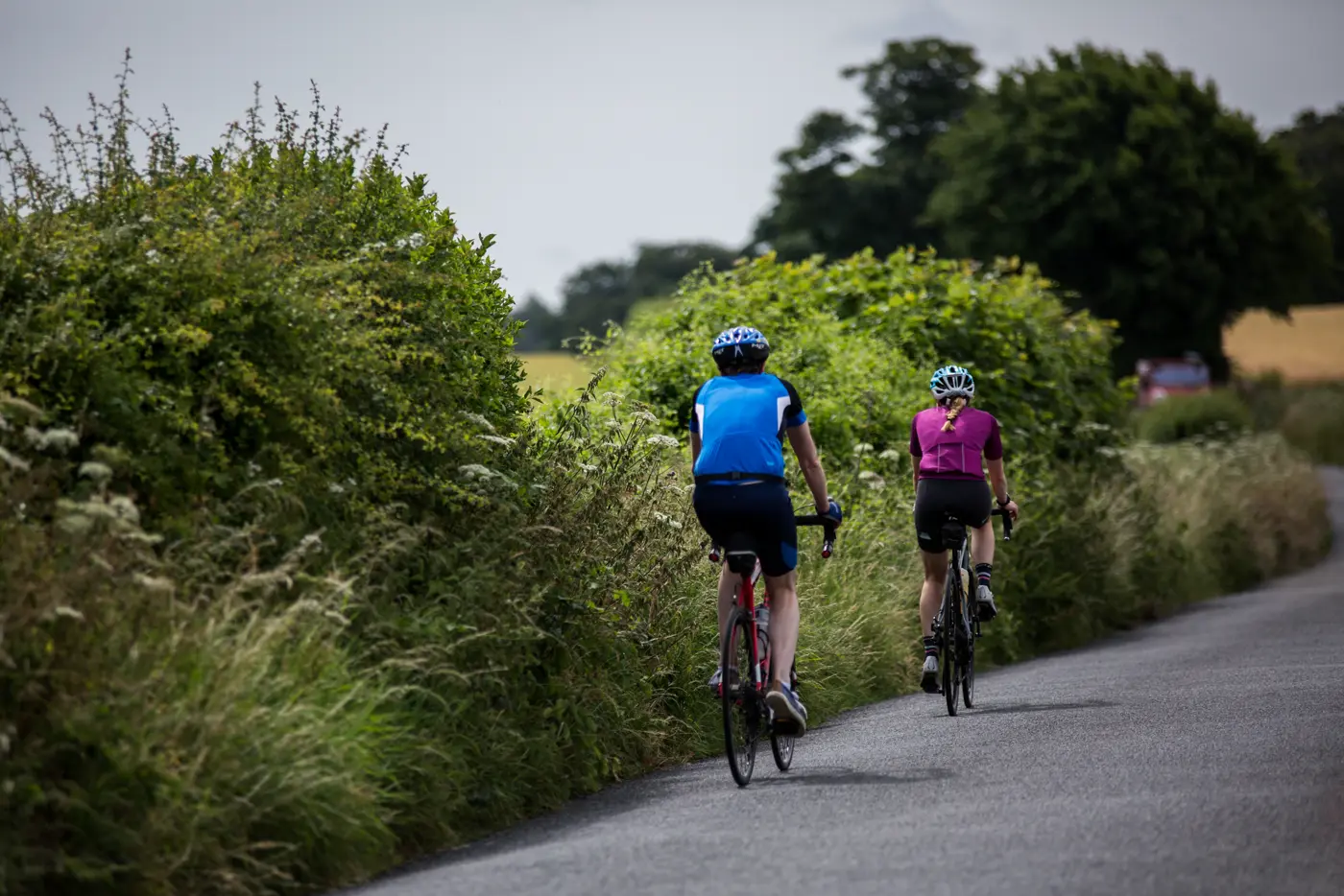 Investec riders cycling along a quiet lane between green hedgerows