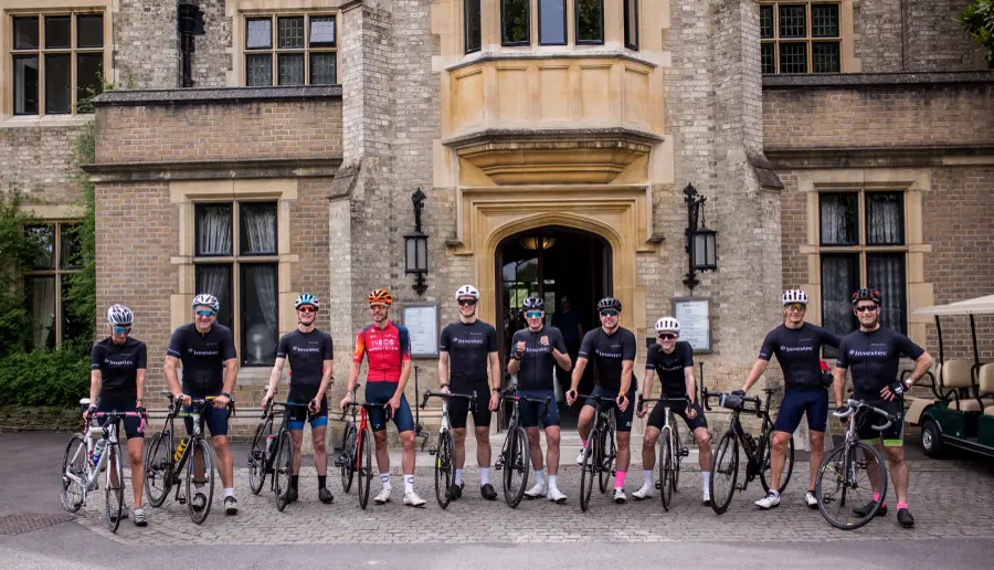 A cycling team with their bikes in front of a stone manor house