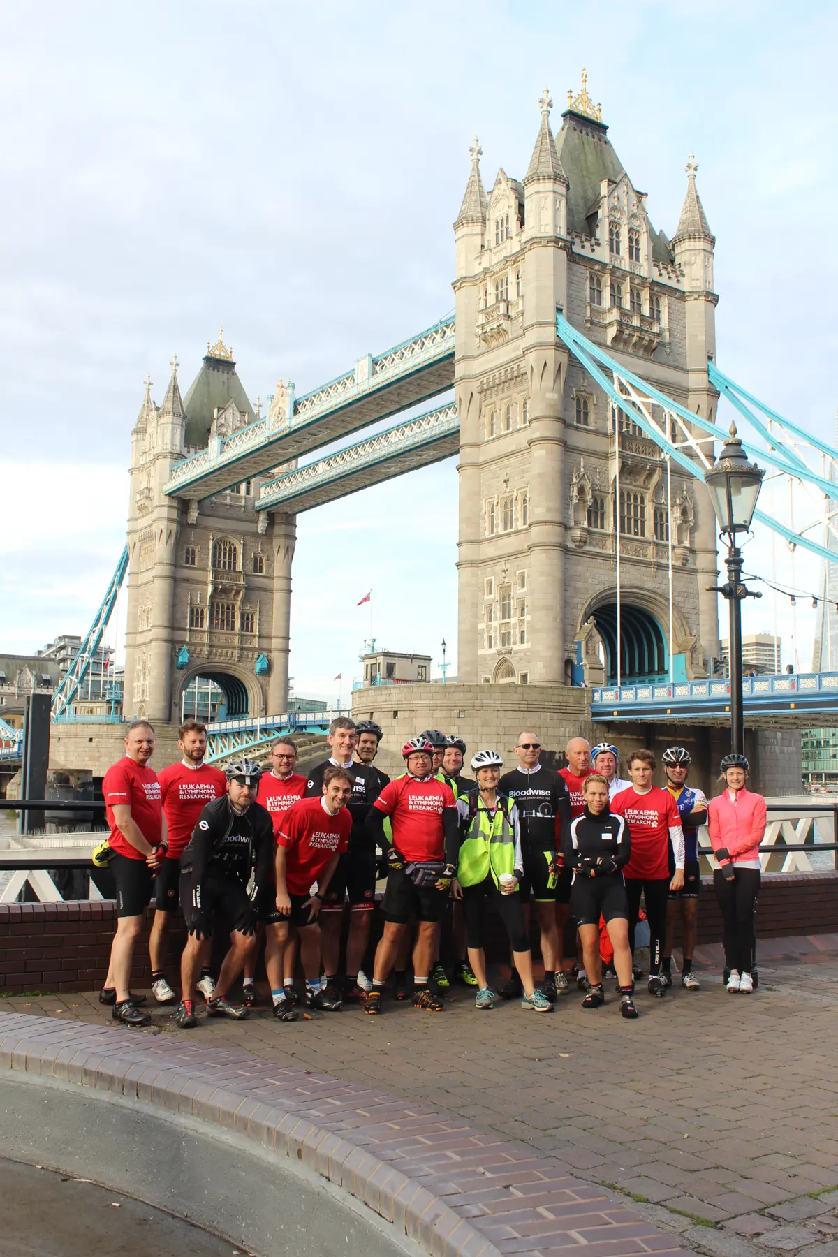 A charity cycling team in matching jerseys with their bikes in front of Tower Bridge in London
