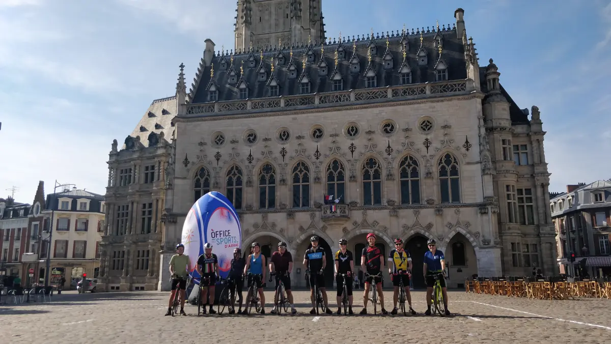 A group of cyclists lined up in front of the ornate Gothic town hall in Arras