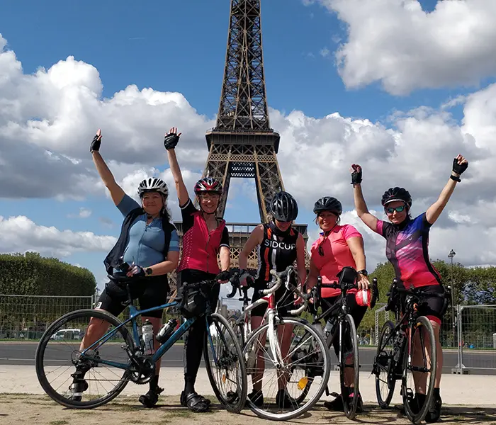 Five cyclists cheering with arms raised in front of the Eiffel Tower