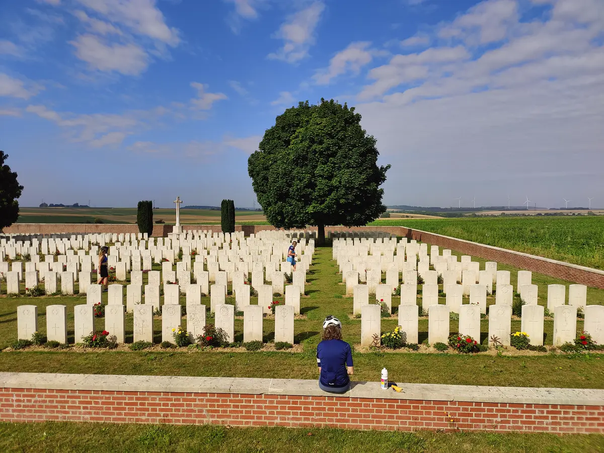 Rows of white headstones in a First World War cemetery, with a cyclist sitting quietly on the wall