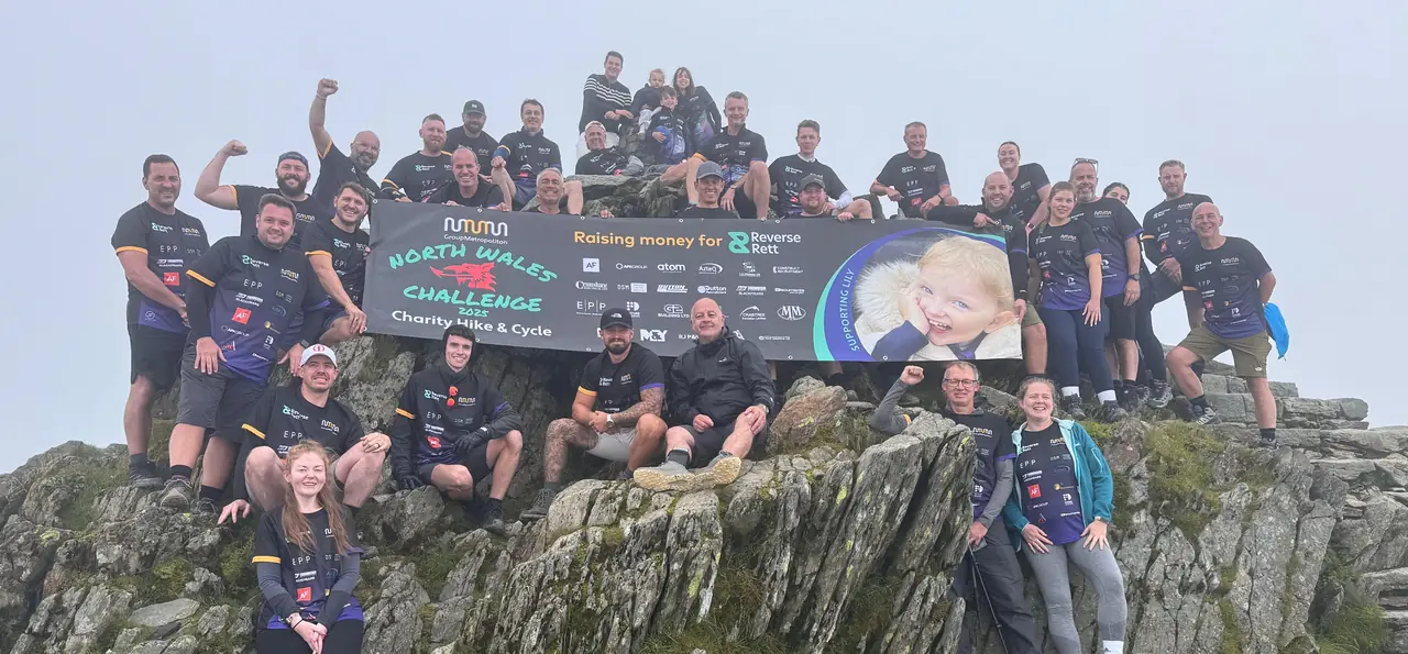Group Metropolitan charity challenge team celebrating on the summit of Yr Wyddfa (Snowdon) with their Reverse Rett banner